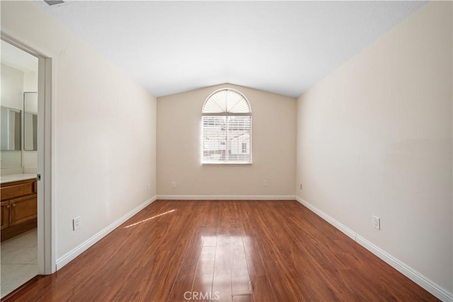 empty room featuring lofted ceiling, baseboards, and wood finished floors