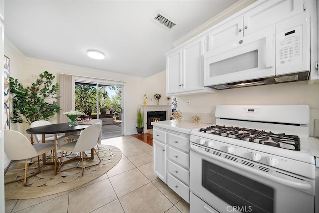 kitchen with light countertops, visible vents, white cabinets, a warm lit fireplace, and white appliances