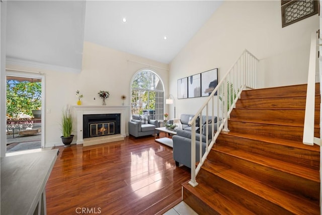 living room featuring high vaulted ceiling, recessed lighting, wood finished floors, stairs, and a glass covered fireplace