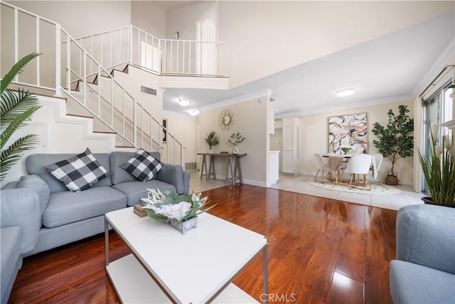 living room featuring visible vents, a high ceiling, ornamental molding, wood finished floors, and stairs