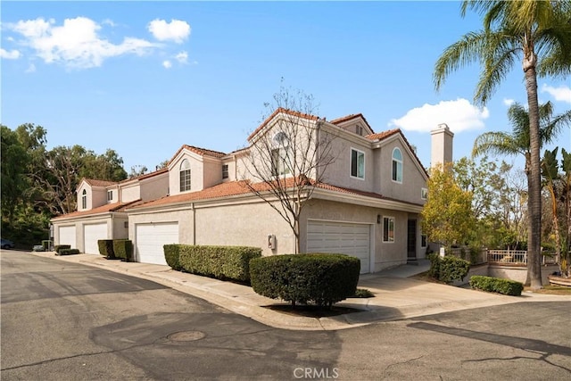 townhome / multi-family property with a garage, a tiled roof, and stucco siding