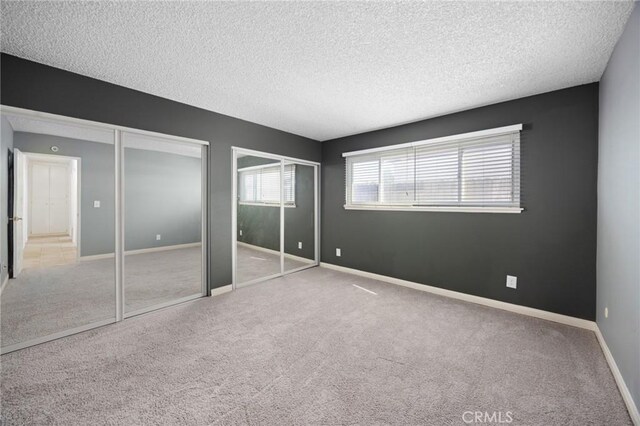 unfurnished bedroom featuring light carpet, a textured ceiling, and two closets