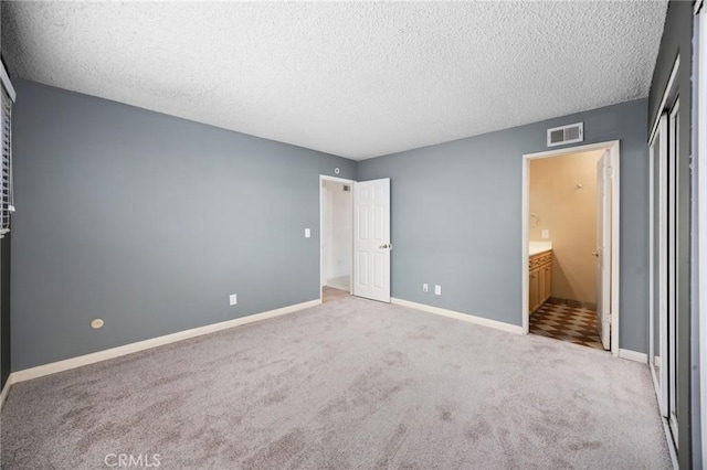 unfurnished bedroom with light colored carpet, connected bathroom, and a textured ceiling