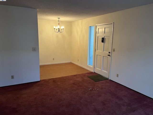 spare room featuring carpet floors, a textured ceiling, and a notable chandelier