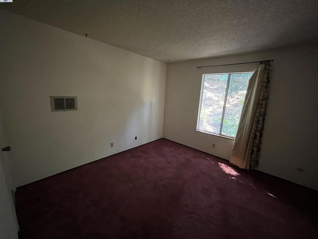 empty room featuring a textured ceiling and dark carpet