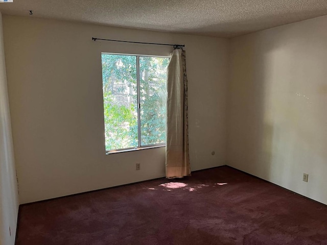 spare room featuring dark carpet and a textured ceiling