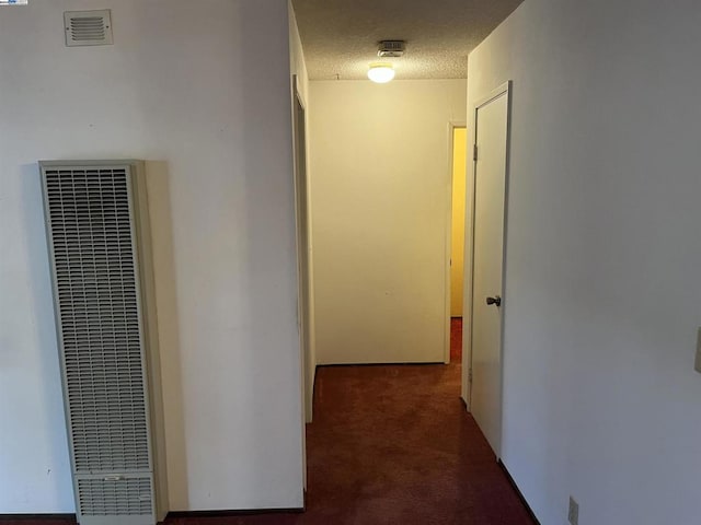 corridor featuring a textured ceiling and dark colored carpet