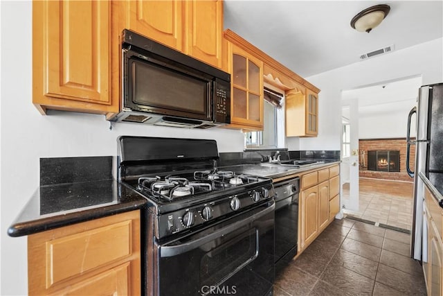 kitchen with sink, a fireplace, dark tile patterned flooring, and black appliances