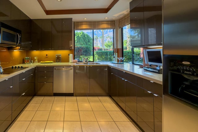 kitchen featuring sink, a tray ceiling, dark brown cabinetry, appliances with stainless steel finishes, and light tile patterned floors