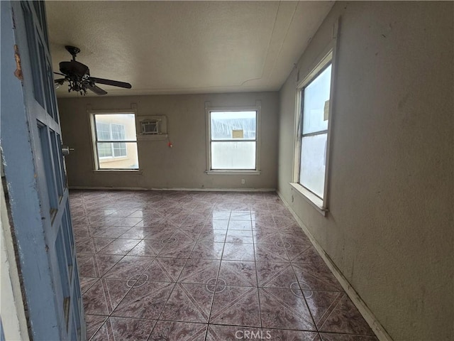 tiled empty room with a textured ceiling, ceiling fan, a wall mounted AC, and a healthy amount of sunlight