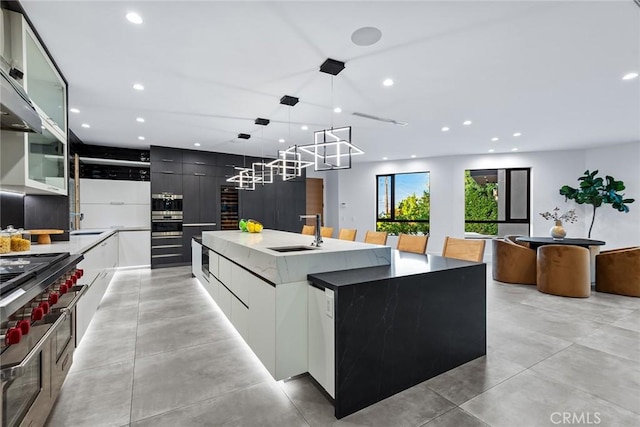 kitchen with a spacious island, pendant lighting, sink, white cabinetry, and range with two ovens