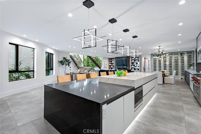 kitchen with ceiling fan, a spacious island, dark stone counters, pendant lighting, and white cabinets