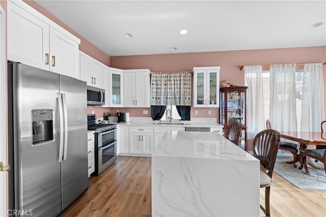 kitchen with appliances with stainless steel finishes, a center island, white cabinetry, sink, and light stone counters