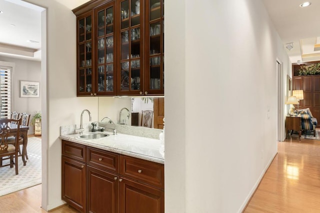 bar with light stone counters, sink, light hardwood / wood-style flooring, and dark brown cabinets