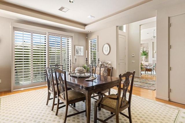 dining space featuring ceiling fan, light wood-type flooring, and a tray ceiling