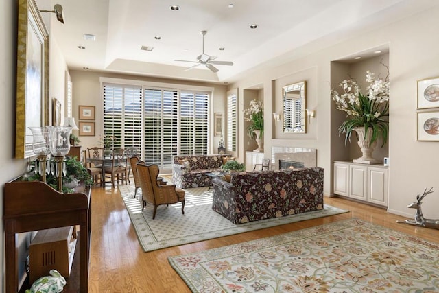 living room with a premium fireplace, ceiling fan, light hardwood / wood-style floors, and a tray ceiling