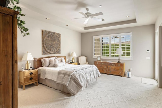 bedroom with ceiling fan, light carpet, and a raised ceiling