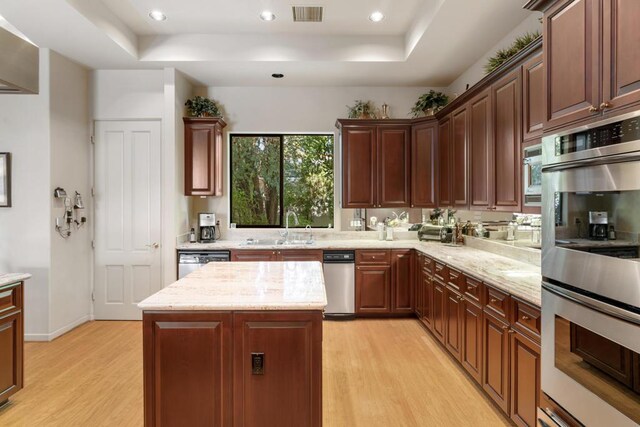 kitchen with a kitchen island, stainless steel appliances, sink, light wood-type flooring, and light stone counters