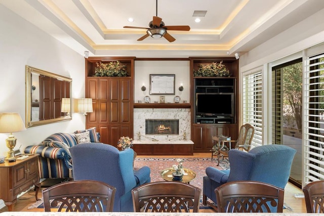 living room with a premium fireplace, a tray ceiling, and ceiling fan