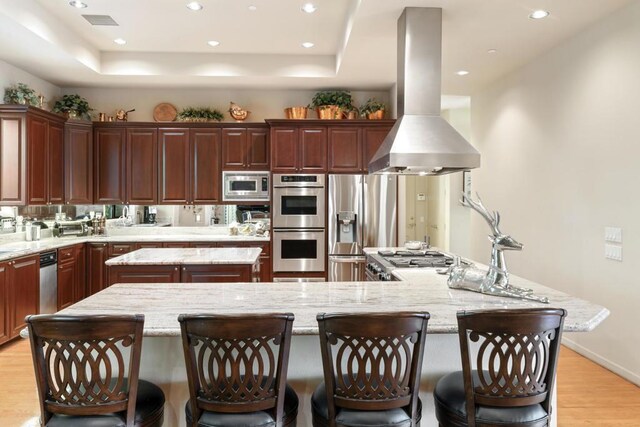 kitchen featuring stainless steel appliances, a kitchen breakfast bar, a large island, light stone counters, and range hood