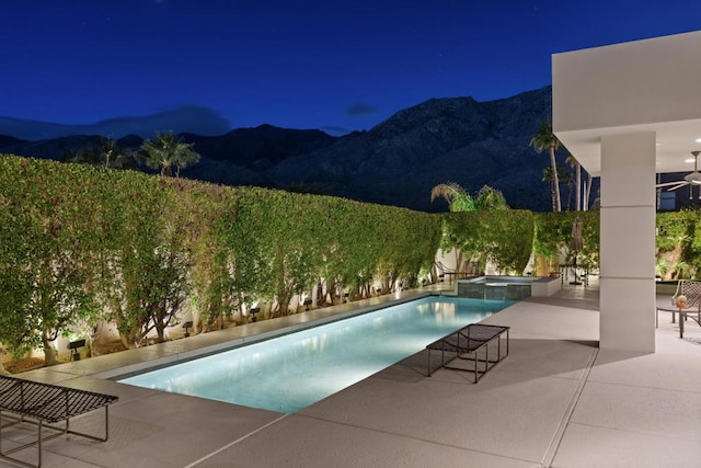 pool at night with a patio area, a mountain view, and an in ground hot tub