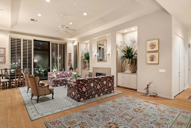 living room featuring ceiling fan, a raised ceiling, and light wood-type flooring