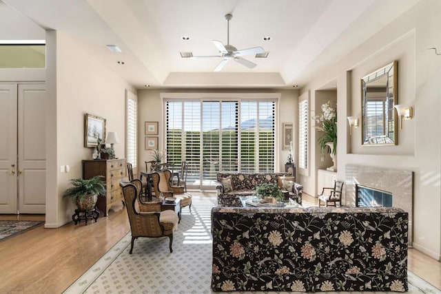 living room with ceiling fan, light hardwood / wood-style flooring, and a raised ceiling