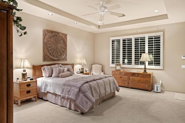 bedroom featuring ceiling fan, light colored carpet, and a raised ceiling