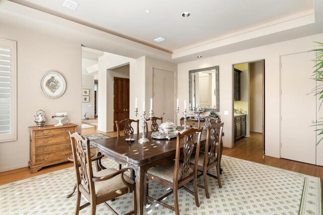 dining area with light wood-type flooring and a tray ceiling