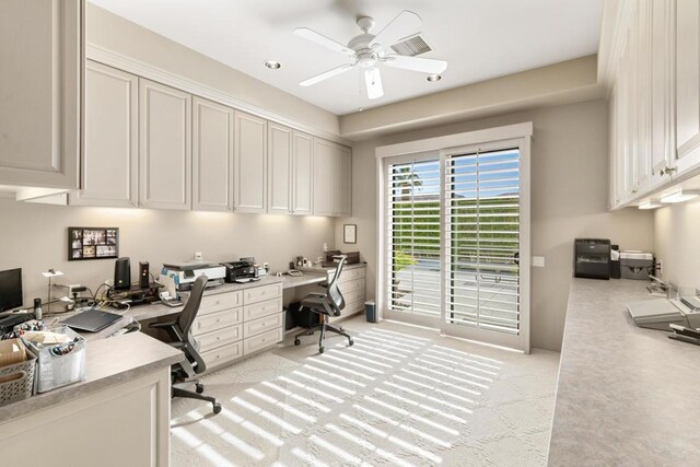 office space featuring built in desk, ceiling fan, and light carpet