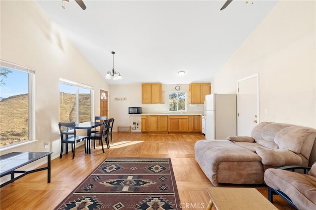 living room with high vaulted ceiling, light wood-style flooring, and ceiling fan with notable chandelier