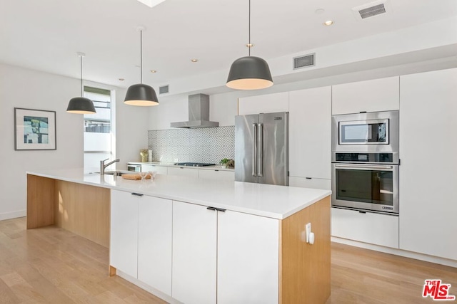 kitchen featuring tasteful backsplash, a spacious island, white cabinetry, appliances with stainless steel finishes, and wall chimney exhaust hood