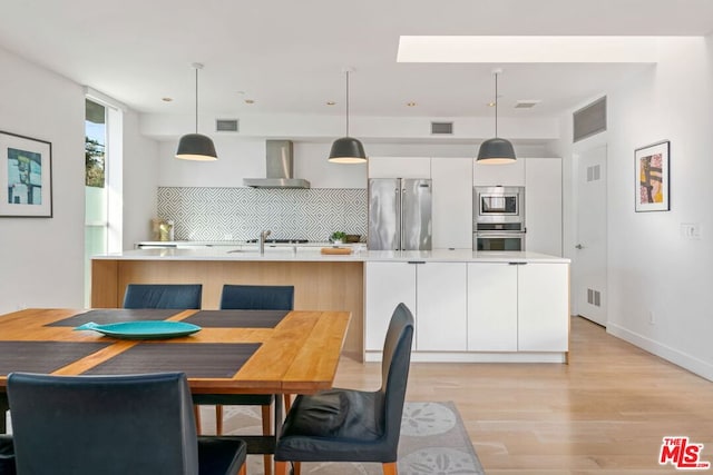 kitchen featuring decorative light fixtures, appliances with stainless steel finishes, wall chimney range hood, and white cabinetry