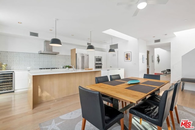 dining area with ceiling fan, sink, beverage cooler, and light hardwood / wood-style floors