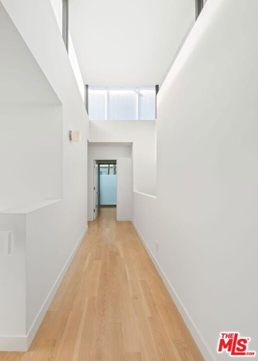 hallway with light hardwood / wood-style floors and a towering ceiling