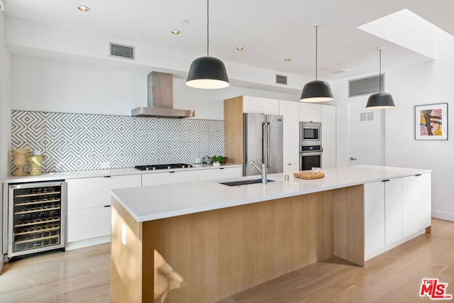 kitchen with wine cooler, white cabinets, wall chimney range hood, and a spacious island