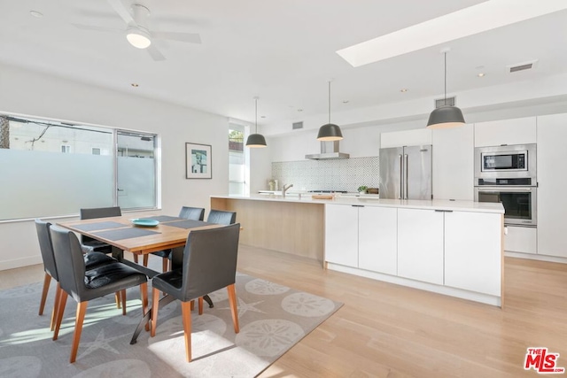 dining area with ceiling fan, a skylight, and light hardwood / wood-style flooring