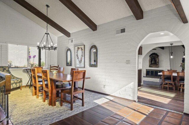 dining area with a fireplace, a notable chandelier, lofted ceiling with beams, wood-type flooring, and a textured ceiling