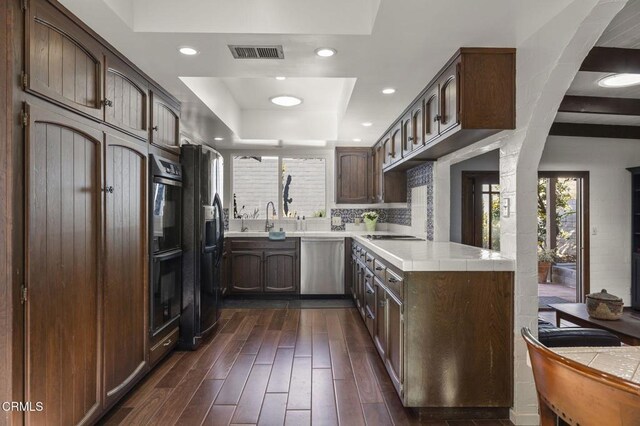 kitchen featuring dishwasher, dark brown cabinets, a tray ceiling, and fridge with ice dispenser