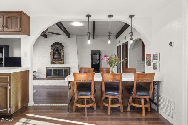 kitchen featuring pendant lighting, a fireplace, dark hardwood / wood-style floors, ceiling fan, and beam ceiling