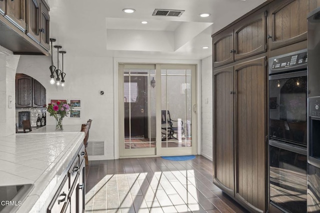 kitchen featuring decorative light fixtures, dark brown cabinetry, dark hardwood / wood-style flooring, and tile counters