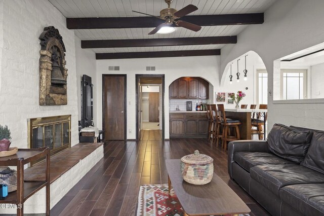 living room featuring ceiling fan, a tile fireplace, and beam ceiling