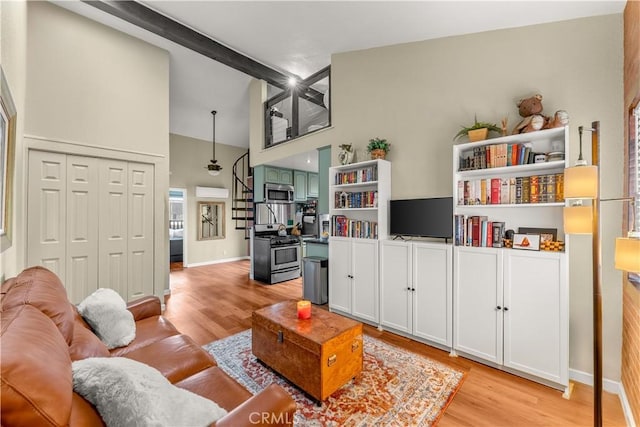 living room featuring light wood-type flooring, beamed ceiling, and a high ceiling