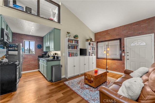 living room with high vaulted ceiling, sink, brick wall, and light hardwood / wood-style floors