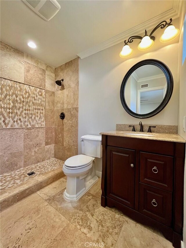 bathroom featuring toilet, a tile shower, crown molding, and vanity