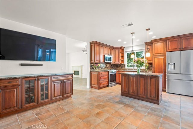 kitchen featuring pendant lighting, backsplash, a center island, dark stone countertops, and stainless steel appliances