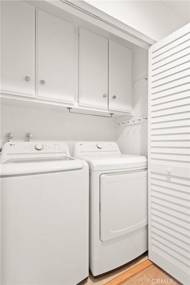 washroom with washer and dryer, cabinets, and light hardwood / wood-style floors