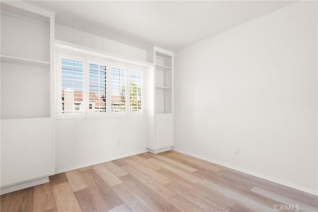 spare room featuring built in shelves and light wood-type flooring