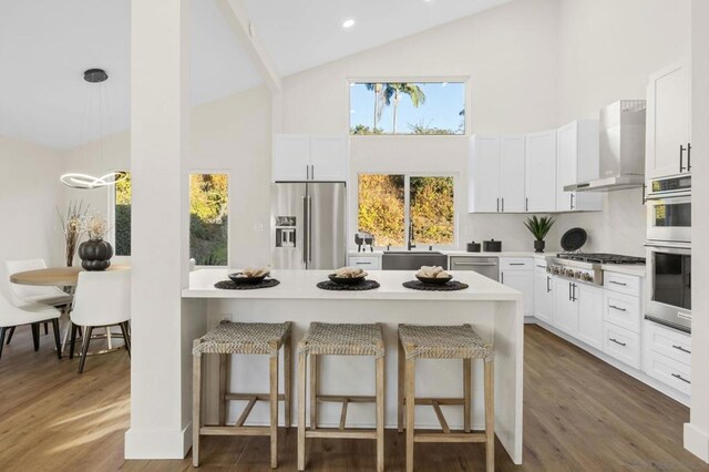 kitchen featuring white cabinetry, wall chimney range hood, stainless steel appliances, and a breakfast bar area