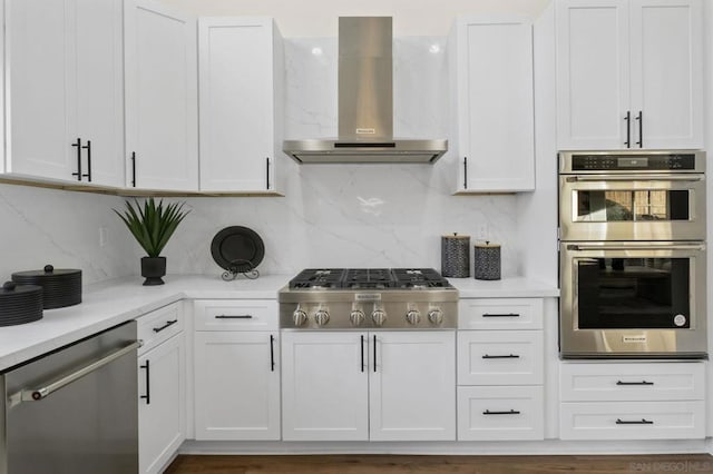 kitchen with stainless steel appliances, wall chimney exhaust hood, white cabinets, and backsplash